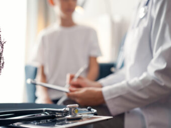 Doctor woman and kid patient at home. The pediatrician fills up medical form, close up. Medicine, healthcare concepts